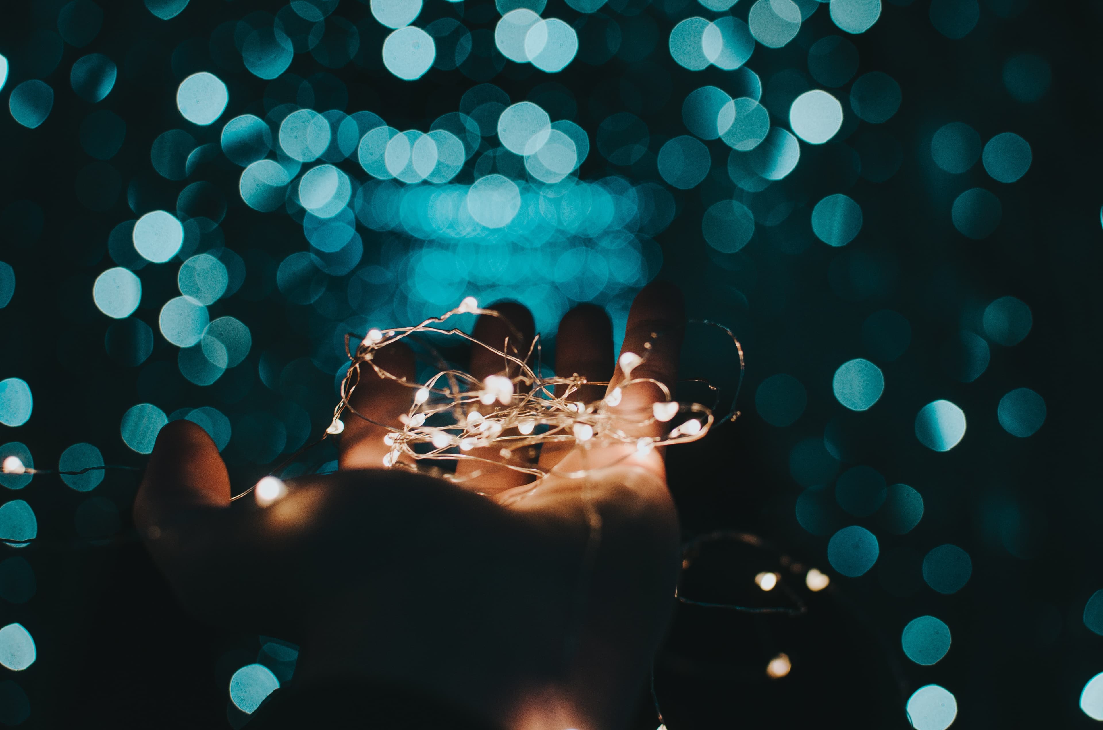 Hand holding string lights with teal bokeh